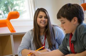 A student teacher works in an elementary aged student in a classroom.